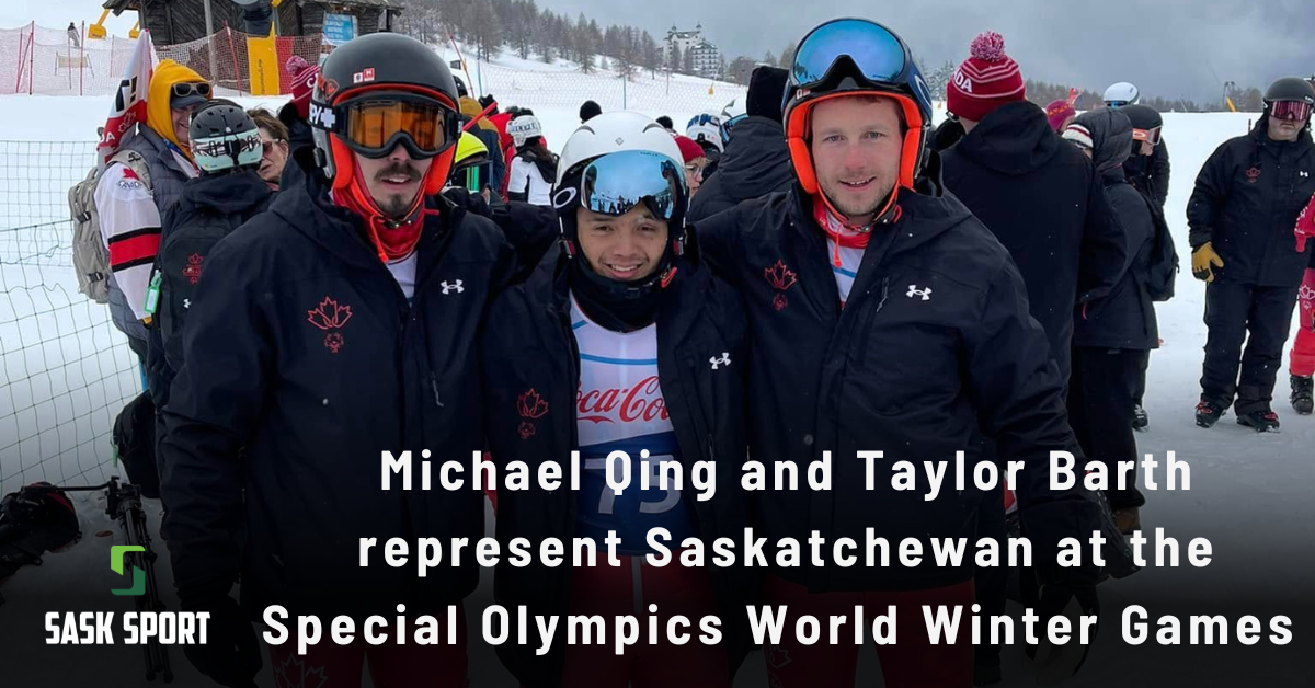 Michael and Taylor stand outside with another athlete in their snow suits and ski goggles. Numerous people are in the background.