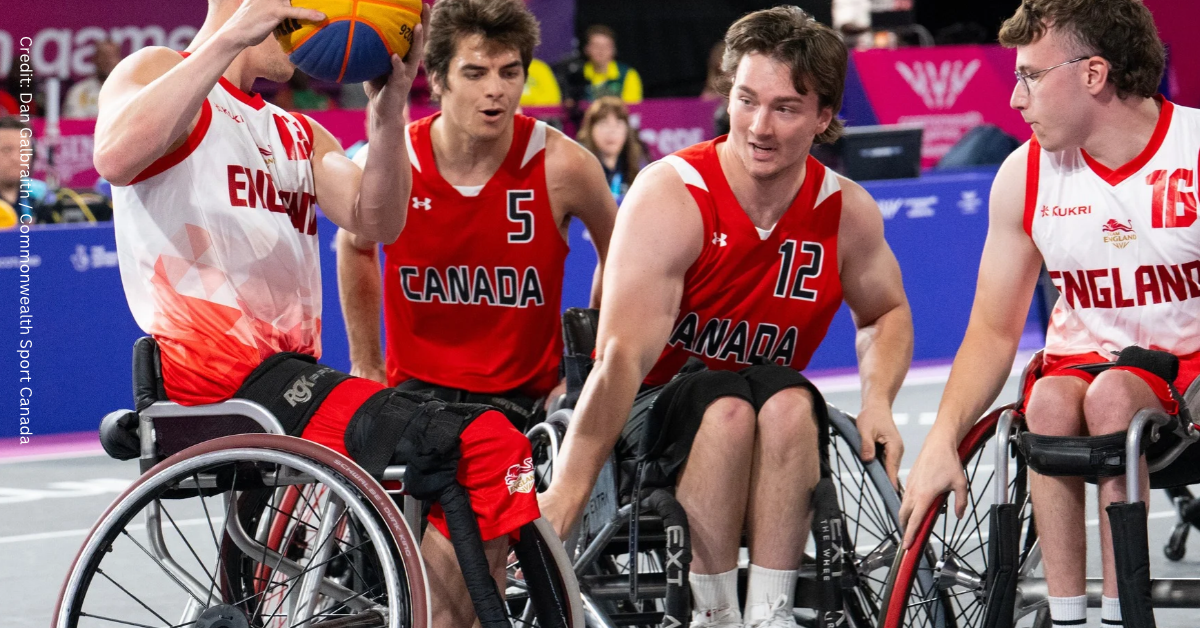 Kyrell Sopotyk and Nik Goncin fight to steal yellow and blue basketball from opponent. Kyrell and Nik are wearing red Canada jersey, while their opponent is in white.